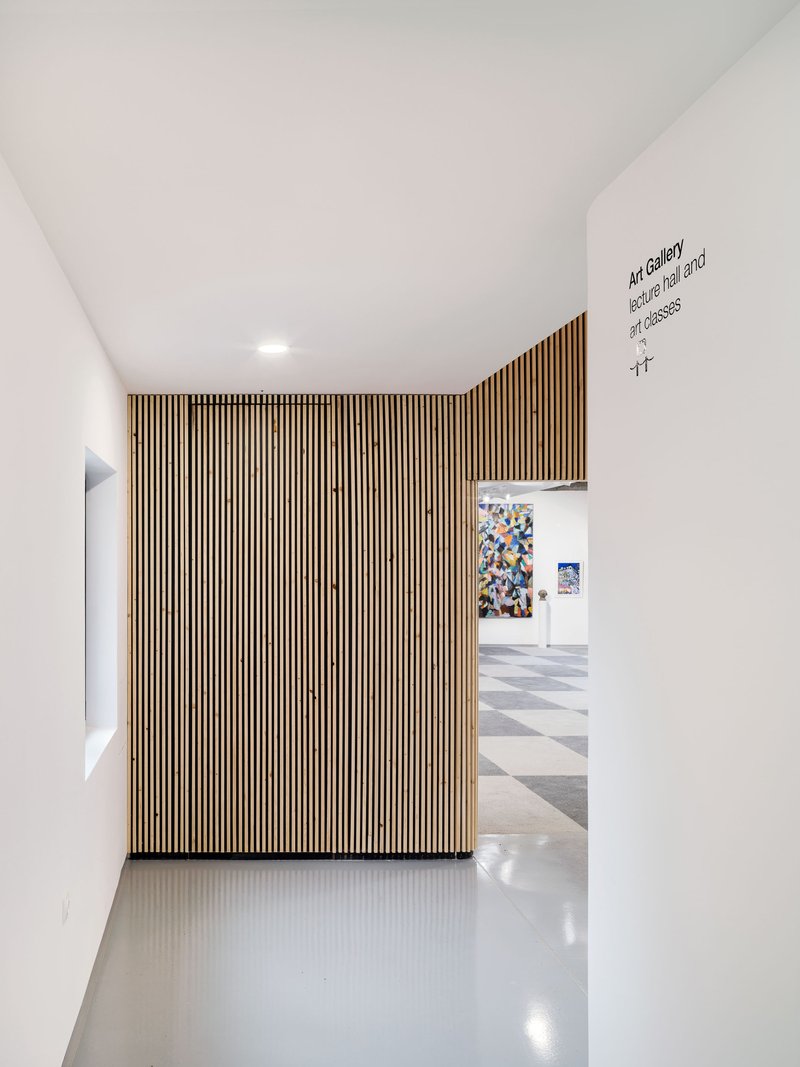 White corridor with vertical timber slat wall leading to gallery space beyond