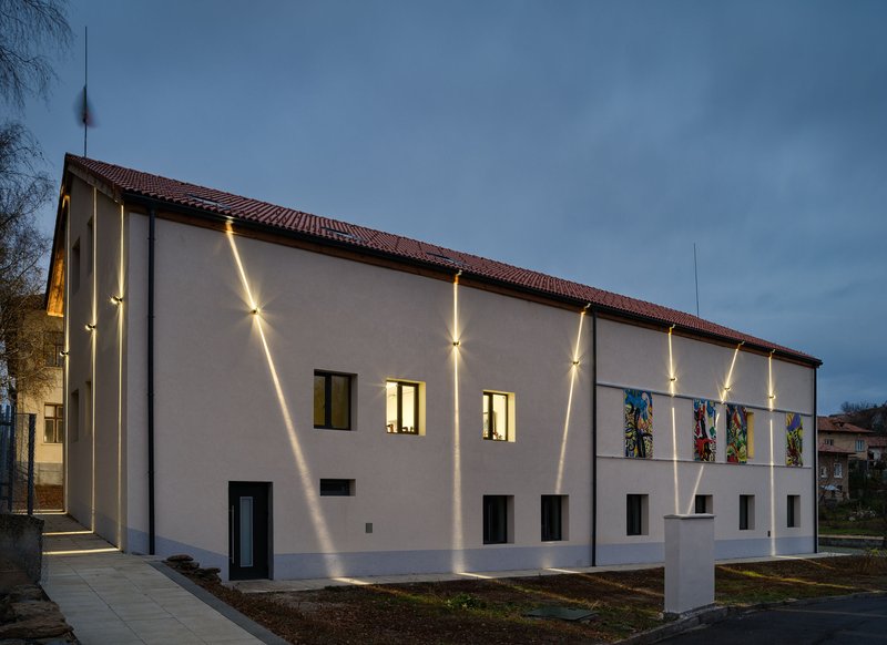 White stucco facade with clay tile roof and vertical strip lighting at dusk