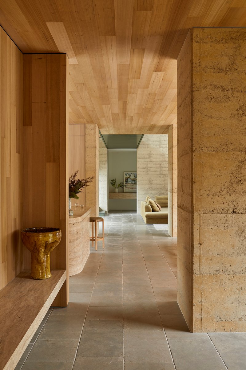 Hallway with timber ceiling planks, rammed earth walls and curved bench with ceramic vessel