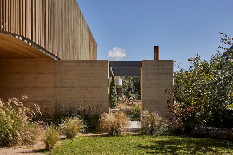 Rammed earth walls framing a courtyard with ornamental grasses under clear sky
