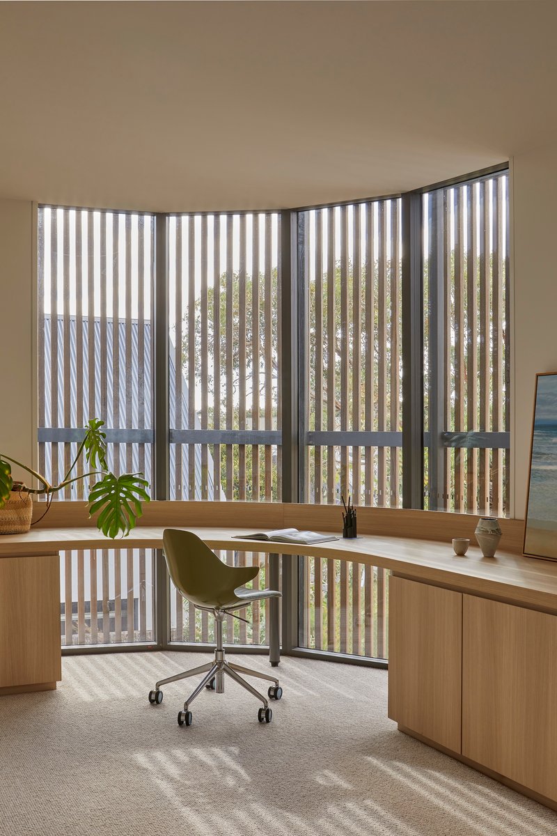Curved study desk at a vertical timber screen filtering dappled light onto the workspace