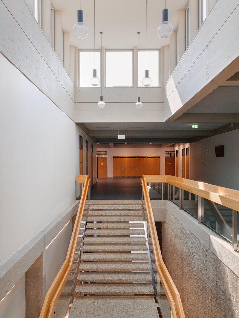 Interior atrium with terrazzo stairs, timber handrails, and pendant lights below a skylight