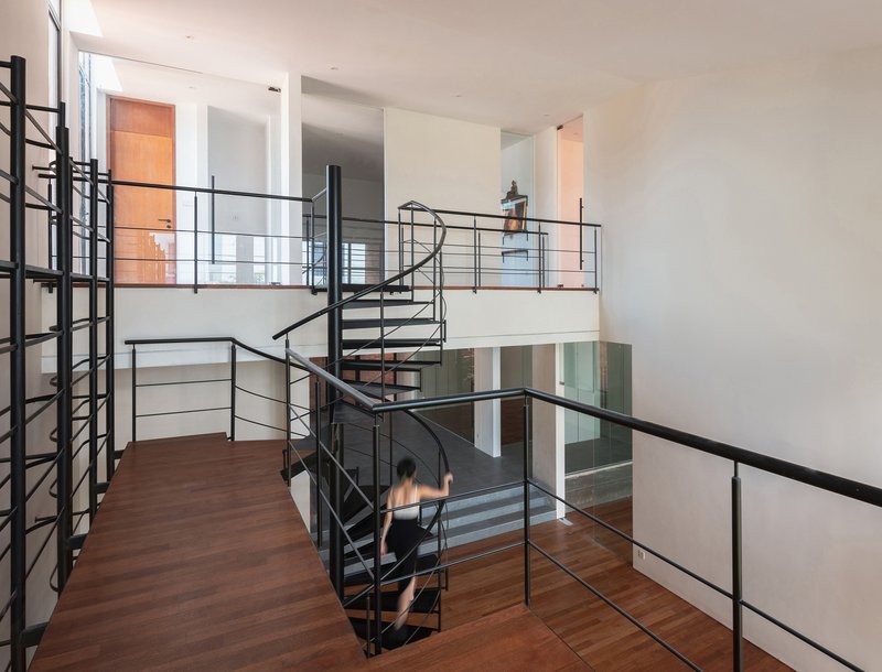 Black steel spiral staircase connecting multiple levels with horizontal railings and wood flooring