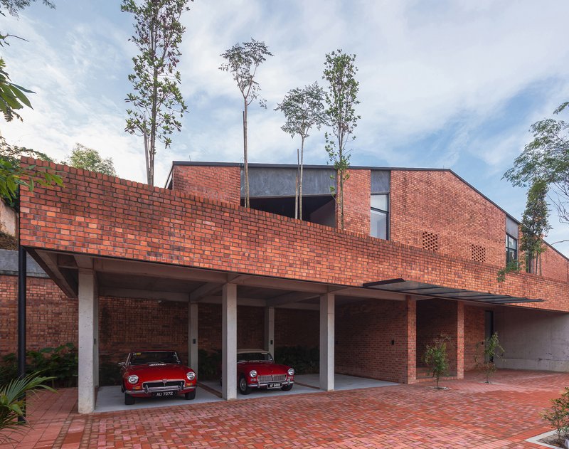 Covered carport with concrete columns beneath red brick facade and rooftop garden with tall trees