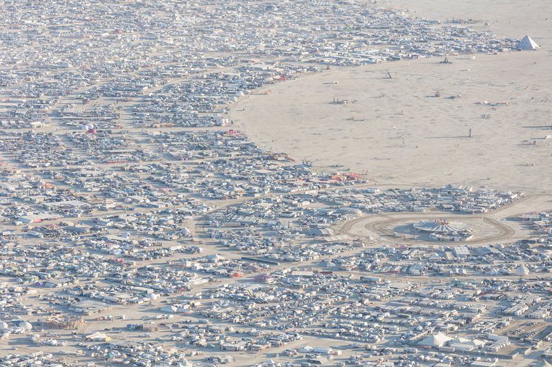 Aerial view of temporary encampment scattered across desert with curving pathways and central installations