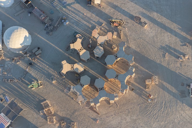 Drone view of hexagonal timber modules clustered on desert playa beside roadway at dawn
