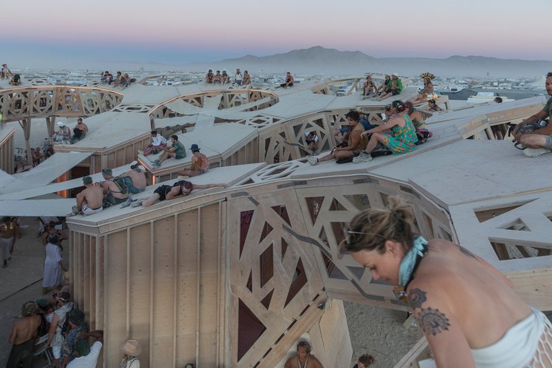 Visitors resting on tiered timber platforms with patterned parapets at twilight with mountains beyond