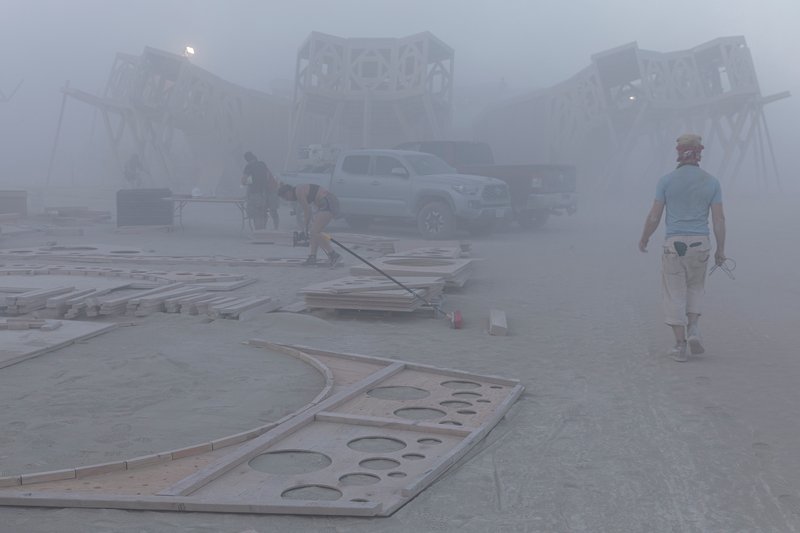 Curved perforated plywood roof panels laid out on the ground during construction in heavy fog