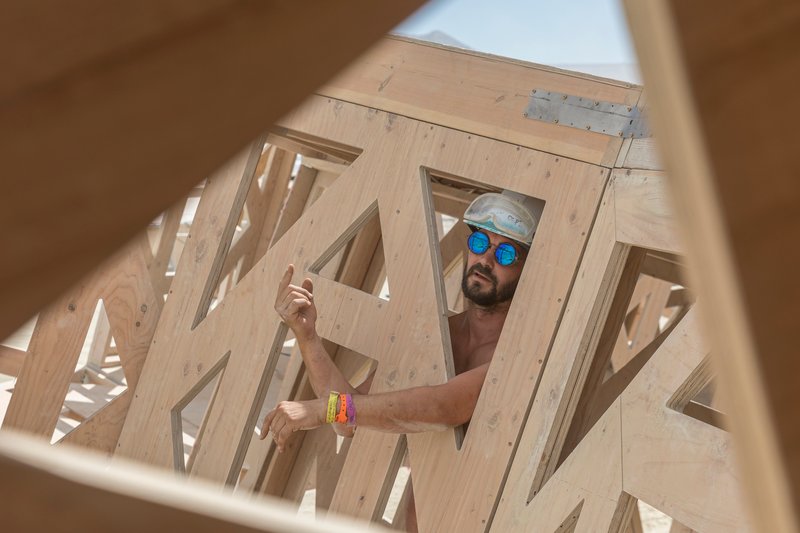 View through triangular plywood openings showing a builder working on the structural framework