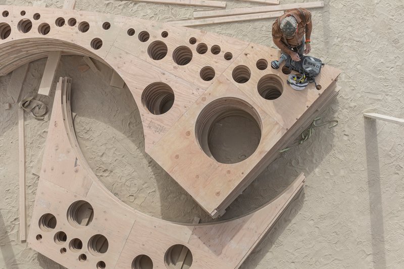 Overhead view of curved plywood panels with circular perforations as a worker applies finish