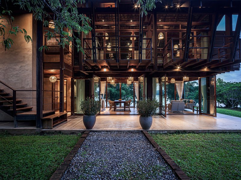 Evening view of raised timber pavilion on columns with pendant lighting and planters at entry