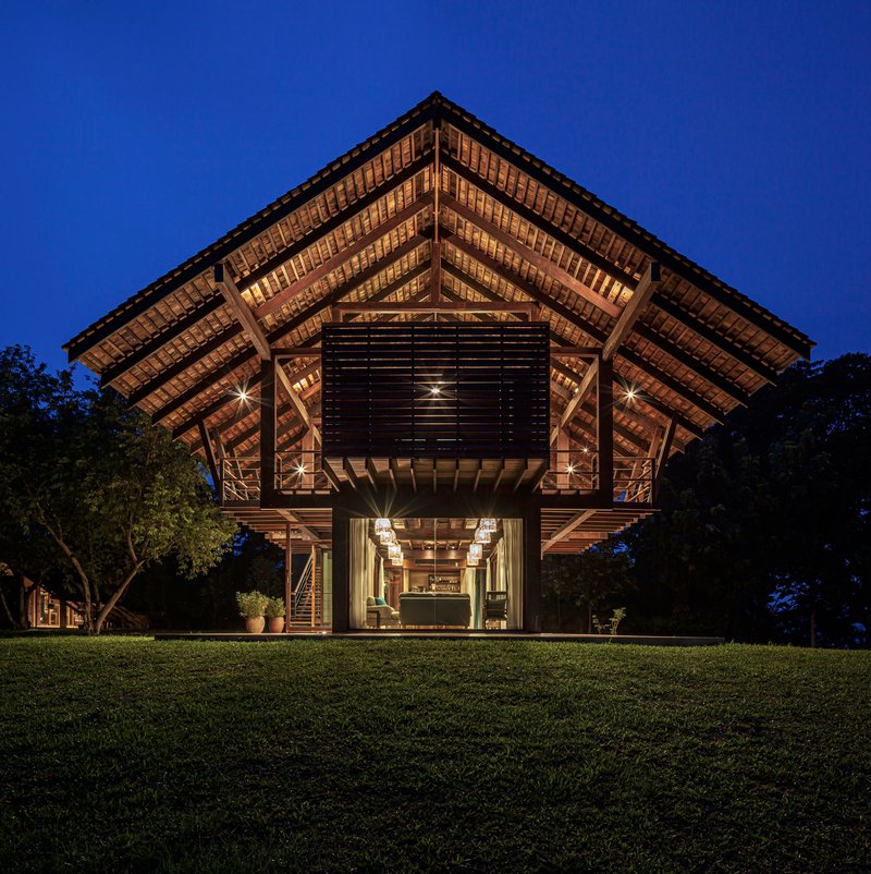 Front elevation showing the timber-framed pavilion with exposed rafters and louvered screen at dusk