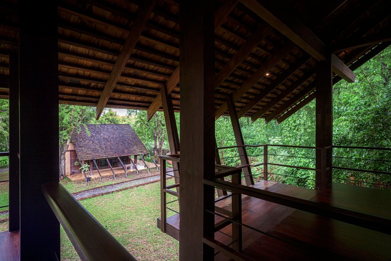 Interior looking through timber columns and steel railings to neighboring gabled structure in garden