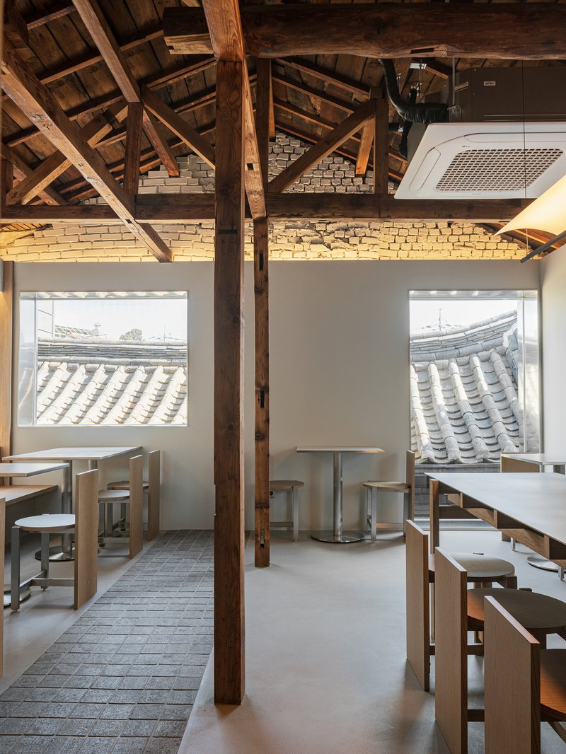 Dining area with exposed timber trusses, grey brick walls, and windows overlooking traditional tile roofs