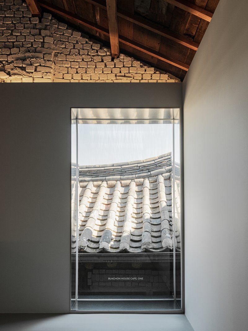 Framed window view of curved ceramic roof tiles beneath exposed timber rafters and grey brick