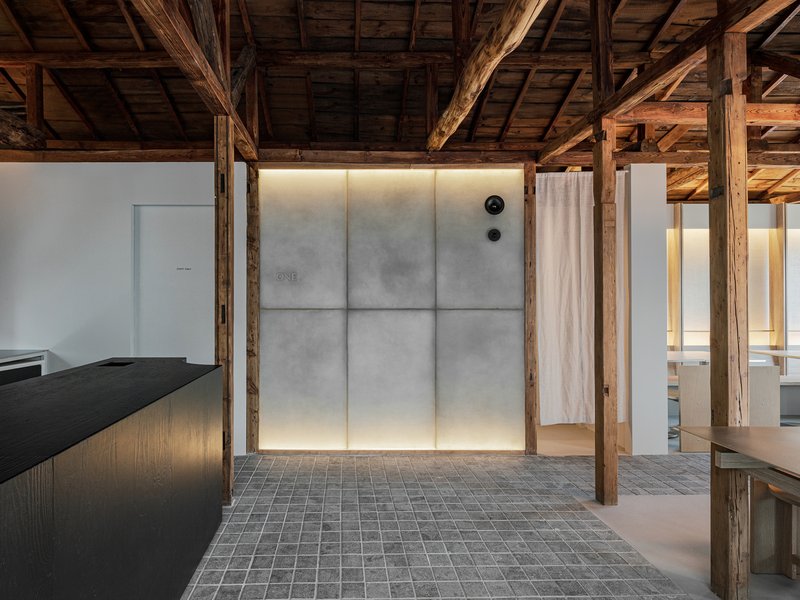 Backlit translucent wall panels with concealed cove lighting surrounded by preserved timber posts and grey brick flooring