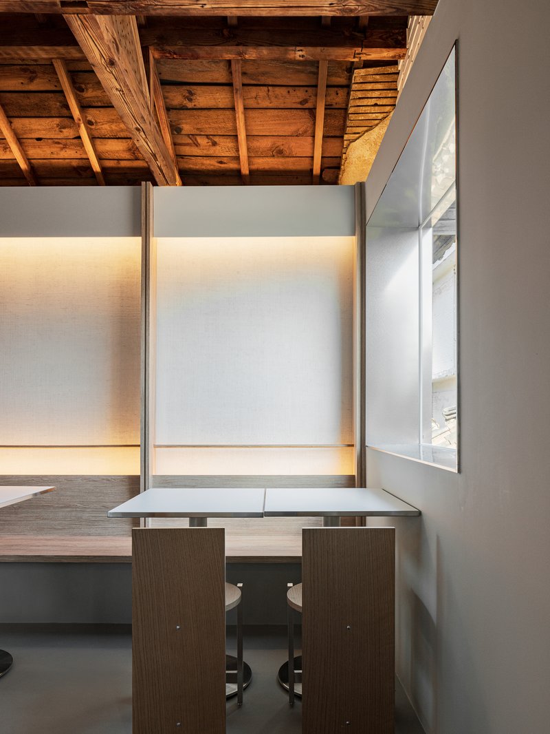 Close-up of a corner table beneath backlit wall panels and weathered timber ceiling joists casting shadows