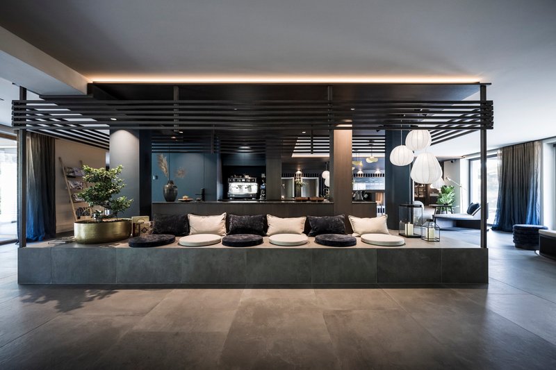 Hospitality bar with horizontal slatted canopy, dark stone counter and pendant lighting under grey ceiling