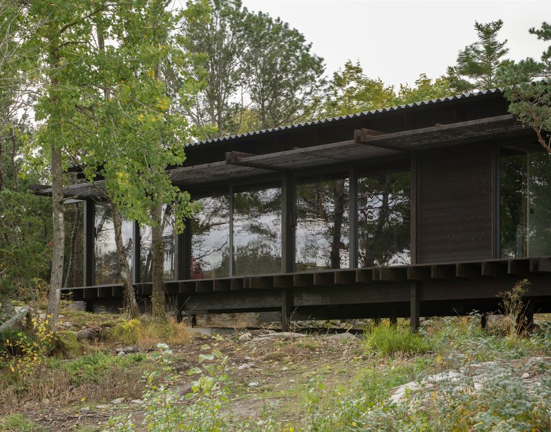 Lakeside elevation showing the raised timber deck and full-height glazing beneath the corrugated metal overhang