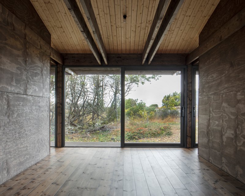 Interior view with exposed timber beam ceiling, marbled plywood walls and floor-to-ceiling windows overlooking vegetation