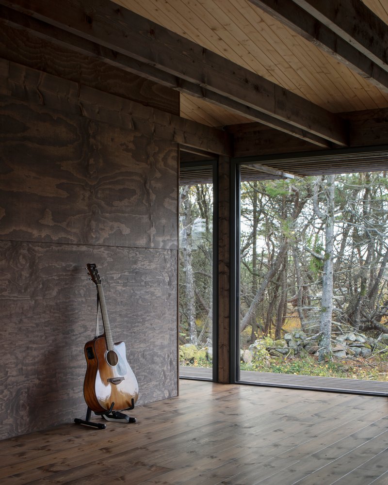 Corner of room with acoustic guitar leaning against marbled plywood wall beside glazed door to landscape