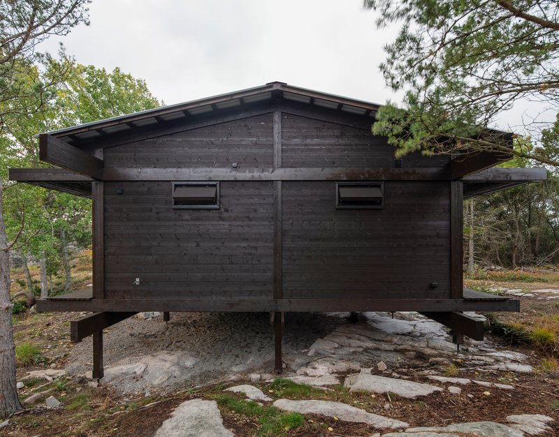 Blackened timber cabin elevated on concrete pillar footings above exposed granite bedrock