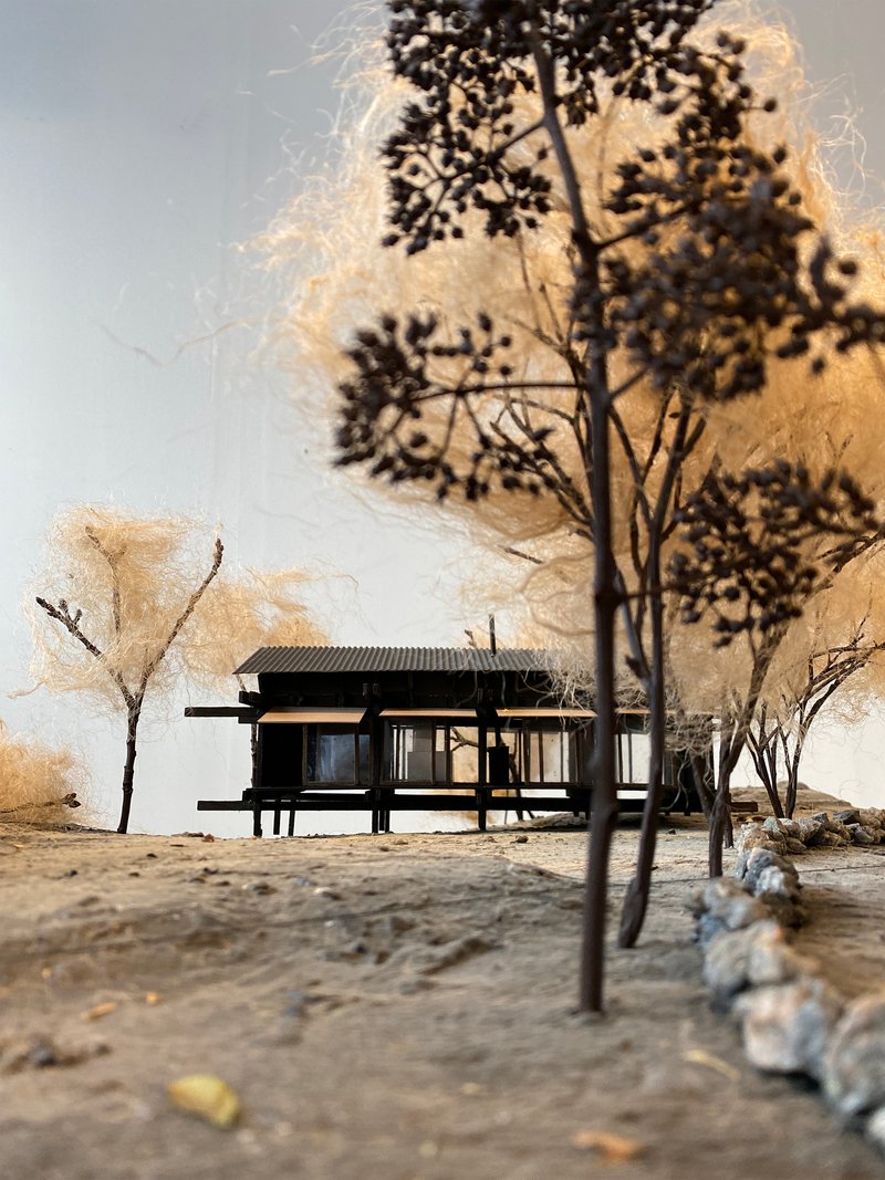 Physical model showing a low pavilion with horizontal roof among miniature trees and textured ground
