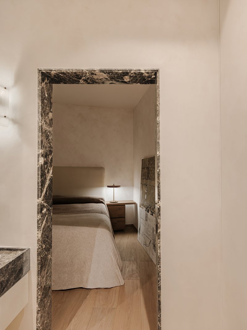 Bedroom viewed through a dark veined marble door frame with nightstand and lamp