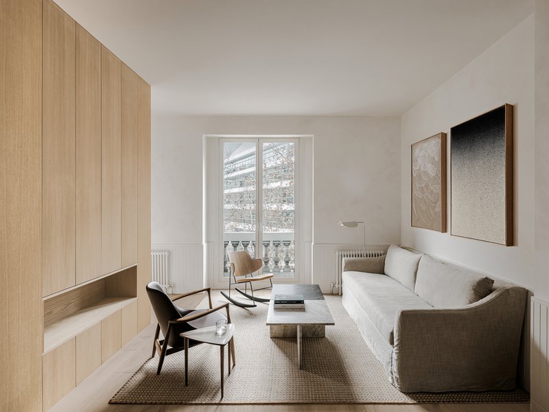 Living room with tall window overlooking winter street, light timber joinery and textured rug