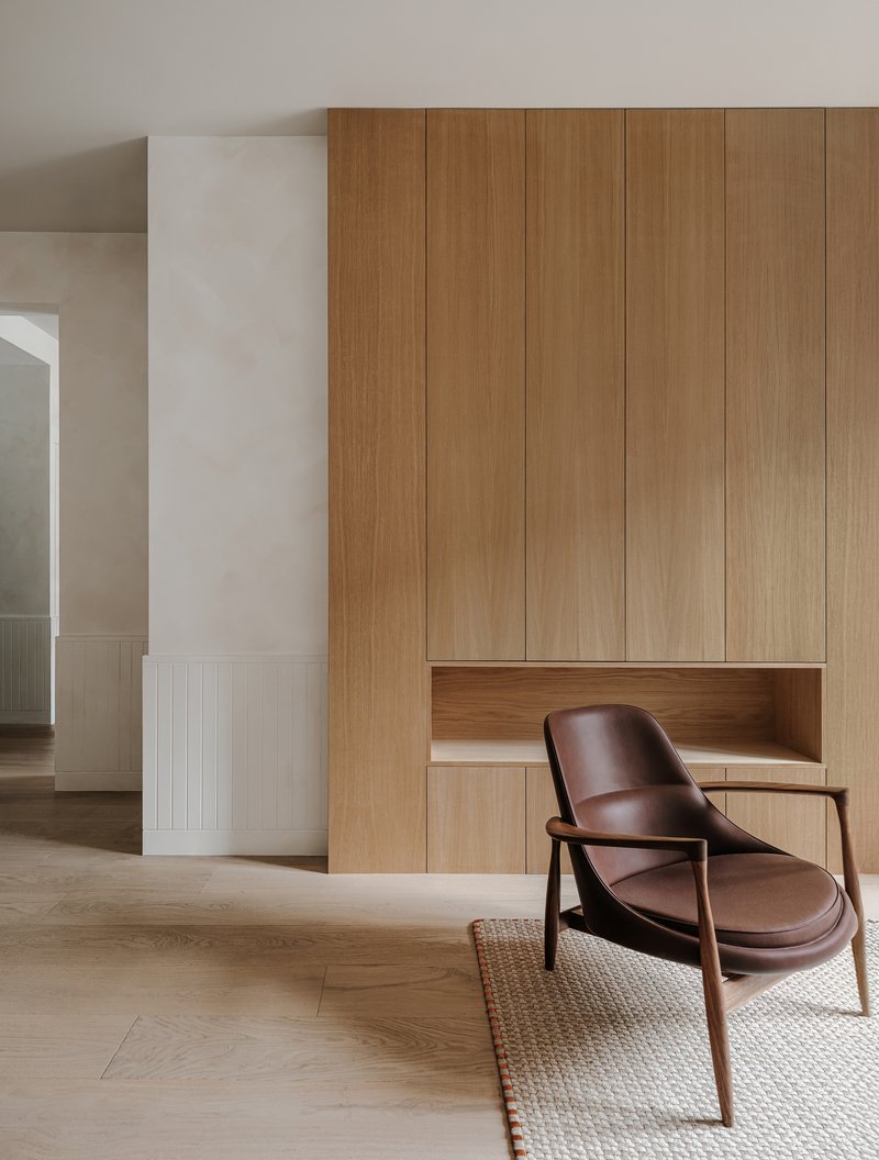Detail of floor-to-ceiling timber cabinetry with horizontal recess and leather lounge chair