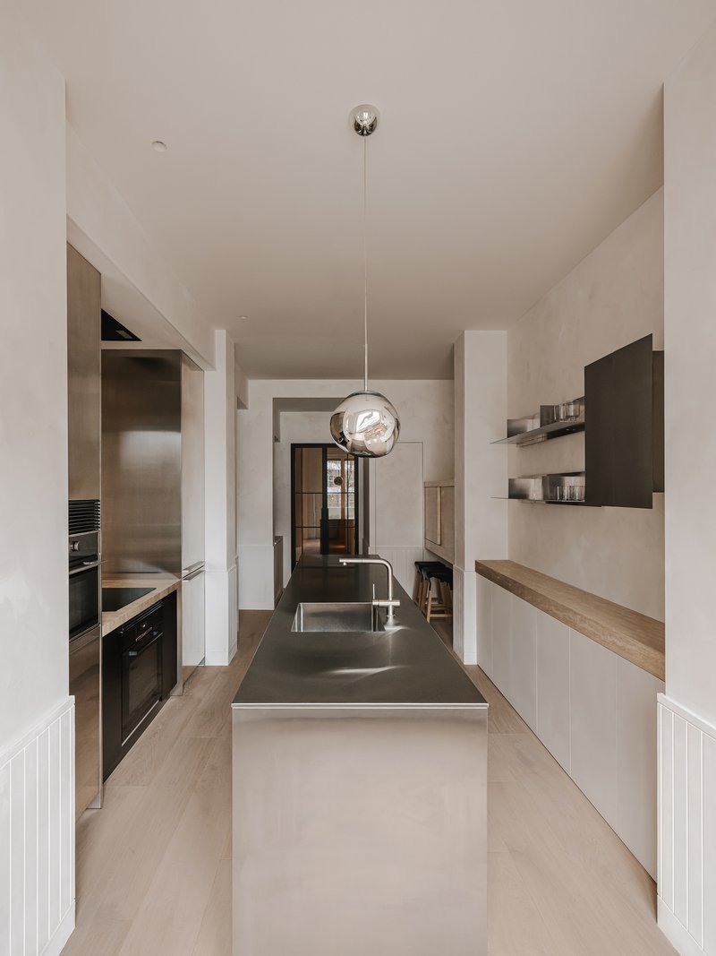 Galley kitchen with stainless steel island, glass pendant and view through to glazed doors