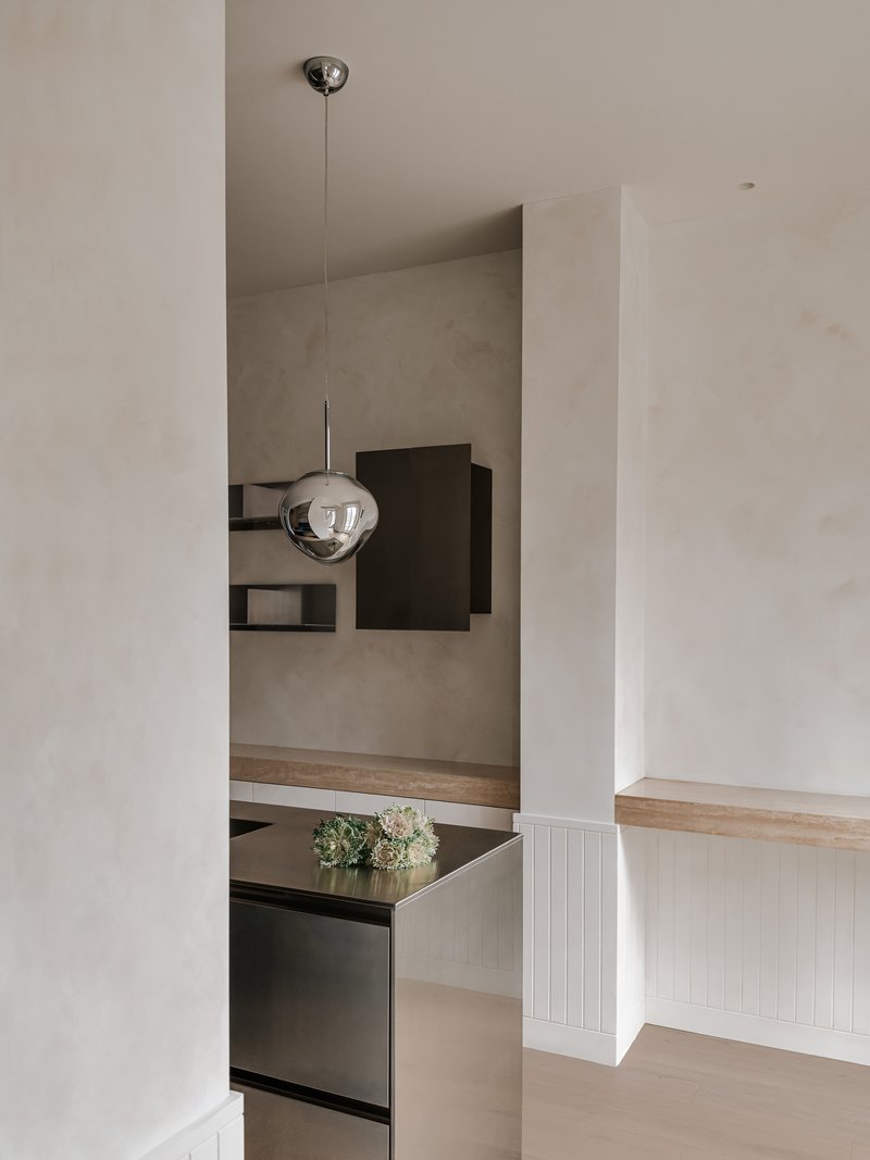 View through a white plastered opening into the kitchen with black island and chrome pendant light