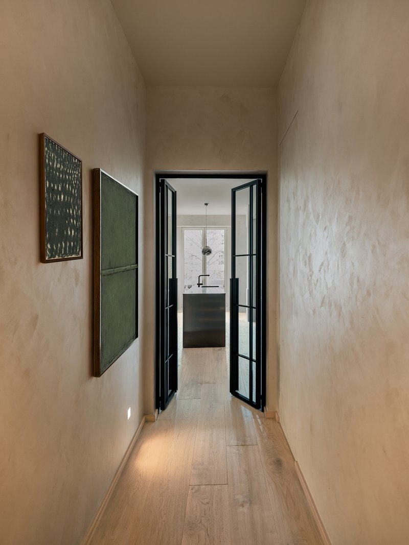 Narrow corridor with limewashed plaster walls leading to the kitchen through black-framed glass doors
