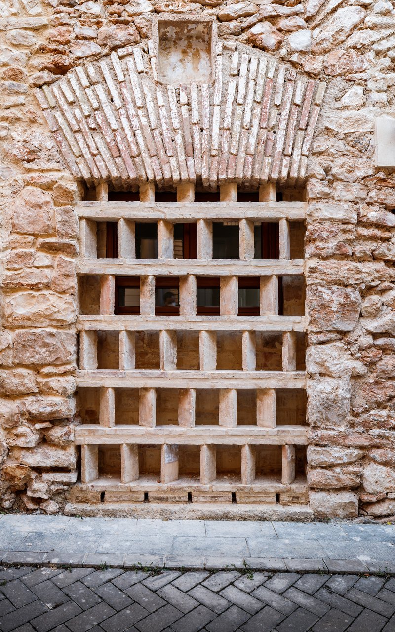 Timber gridded door set within a weathered stone wall above herringbone paving
