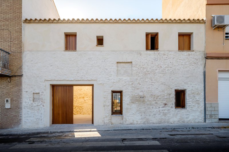 Street view of the white stucco facade with timber-framed openings and terracotta tile roof at dusk