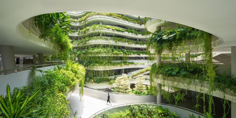 Interior atrium with spiraling planted terraces and cascading vines under a circular skylight with a person walking below
