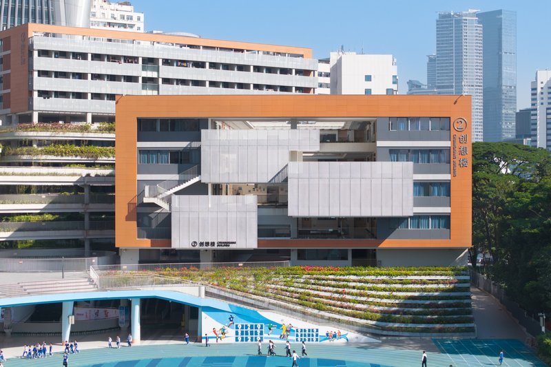 Facade with orange-framed white panels and a terraced amphitheater leading to a teal-paved courtyard with students