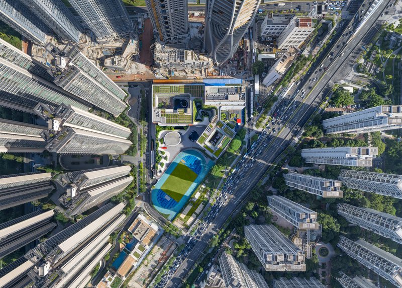 Drone view of the landscaped podium roof with pool and sports field nestled between dense high-rise towers
