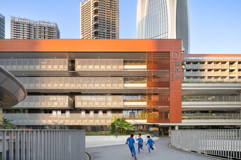 Facade detail showing horizontal orange louvers and glazed galleries with three children running across the foreground plaza