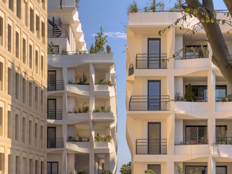 Facade detail showing stacked balconies with metal railings and planters flanked by an existing tree
