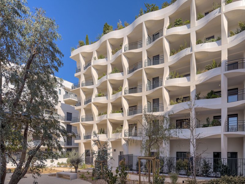 White concrete facade with wavy balcony edges and planters beneath a clear blue sky