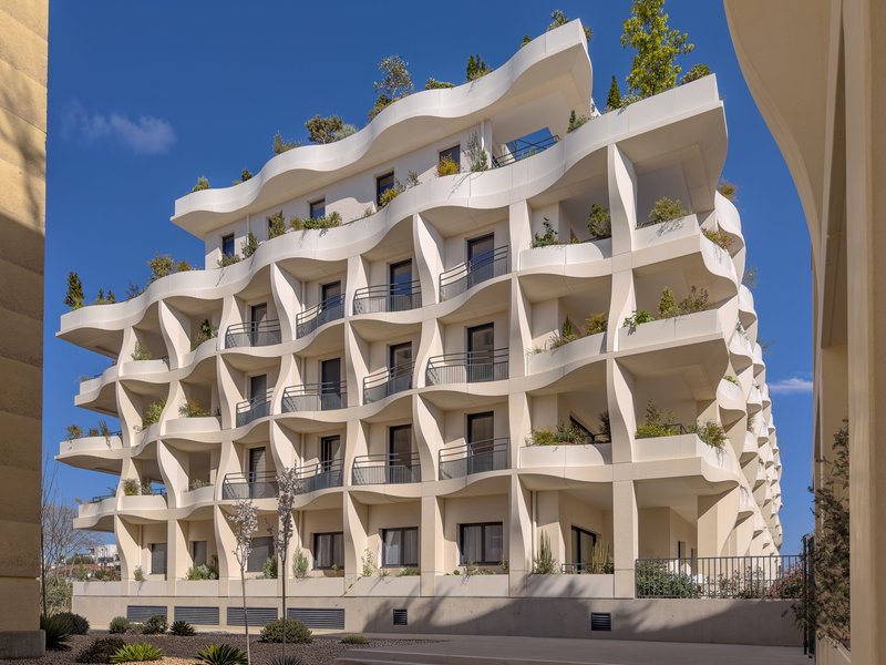 White facade with undulating balconies and rooftop planters under a clear blue sky