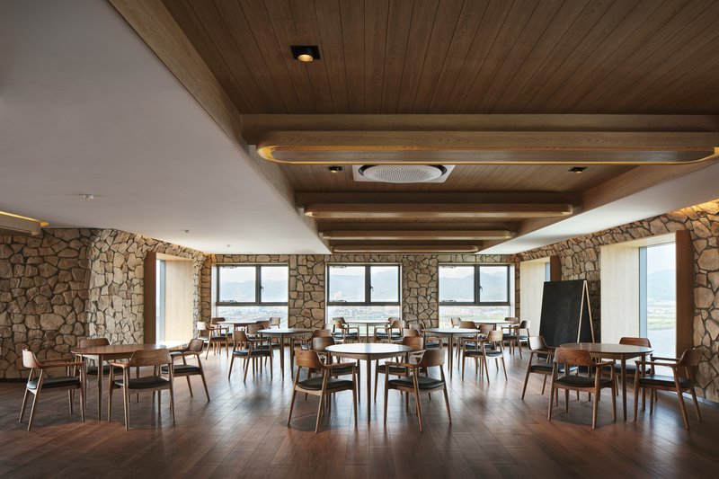 Dining hall with timber-slatted ceiling above white plaster volumes and fieldstone walls with river views