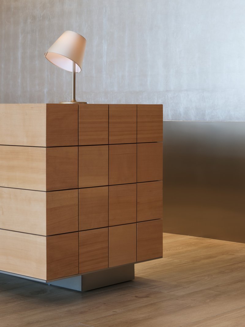 Stepped timber block reception desk with table lamp against a textured grey wall