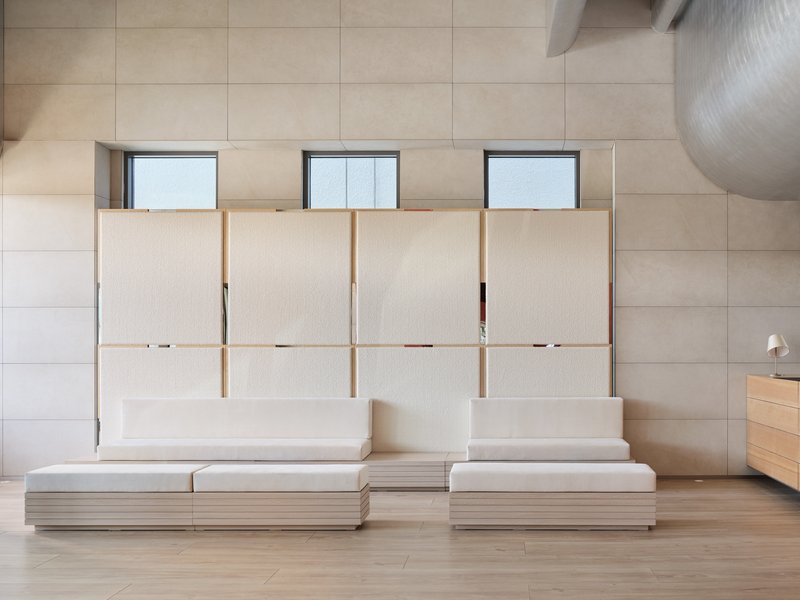 Interior wall with pale wood cabinetry and four translucent sliding panels above a low platform seating arrangement