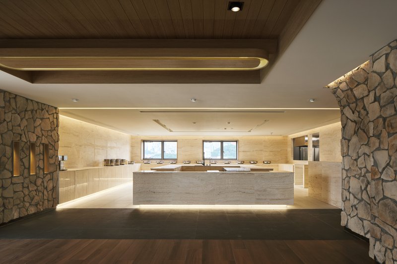 Reception hall with fieldstone columns, timber ceiling beams, and a backlit travertine service counter