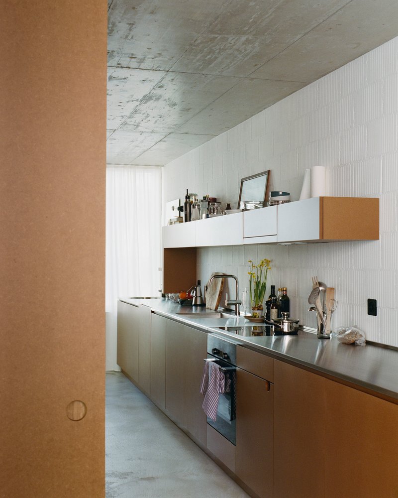 Galley kitchen with stainless steel countertops under an exposed concrete ceiling with daylight