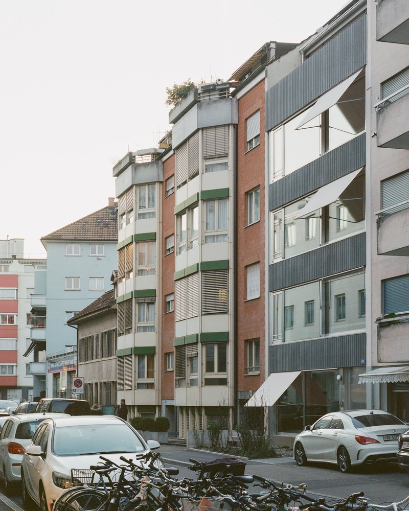 Streetscape showing a mix of residential buildings with metal cladding, brick and balconies with parked cars and bicycles