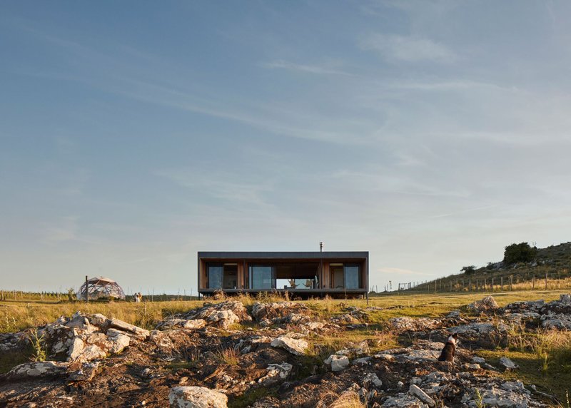 Dark corrugated box volume elevated on a rocky outcrop overlooking dry grassland at dusk