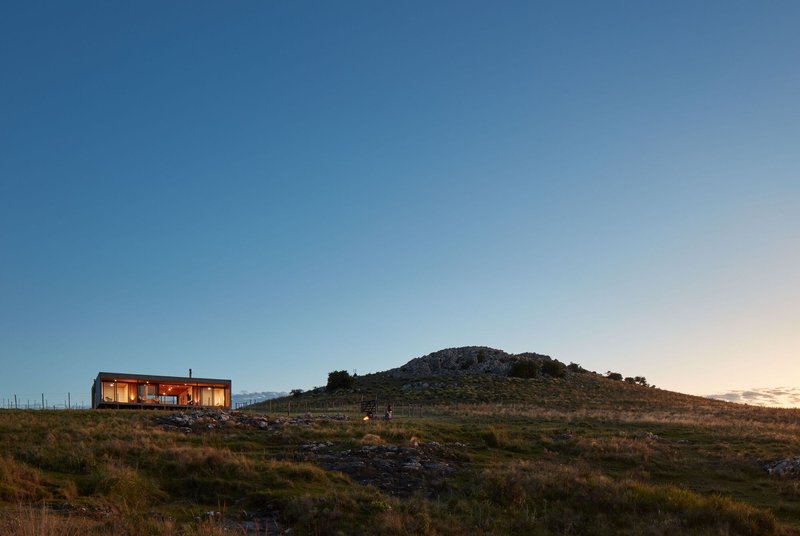 Long view of the illuminated glass volume on a hillside at twilight